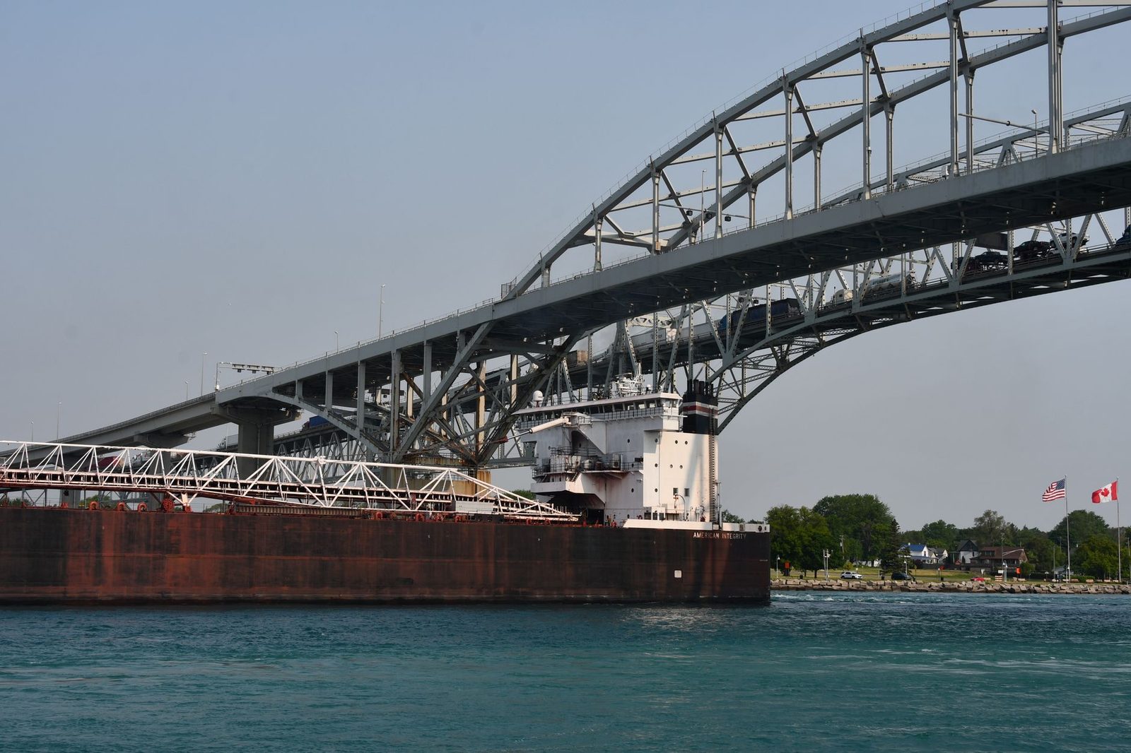 Cargo ship passing under the Blue Water Bridge connecting USA and Canada on a clear day.